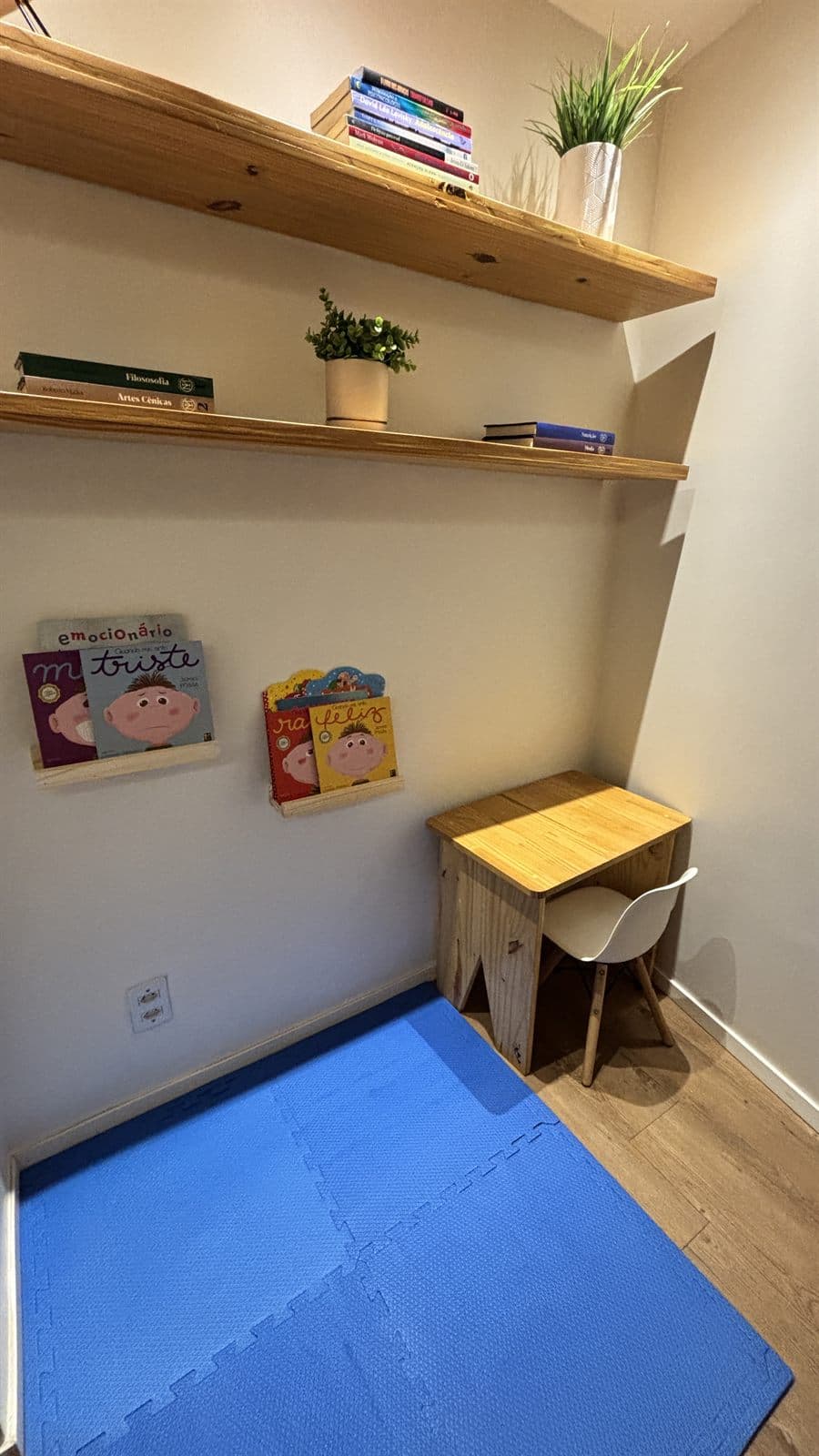 Espaço infantil com prateleiras de livros, mesinha de madeira e tapete emborrachado