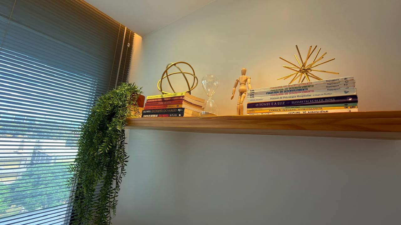 Prateleira com livros de psicologia, ampulheta, manequim de madeira e planta pendente
