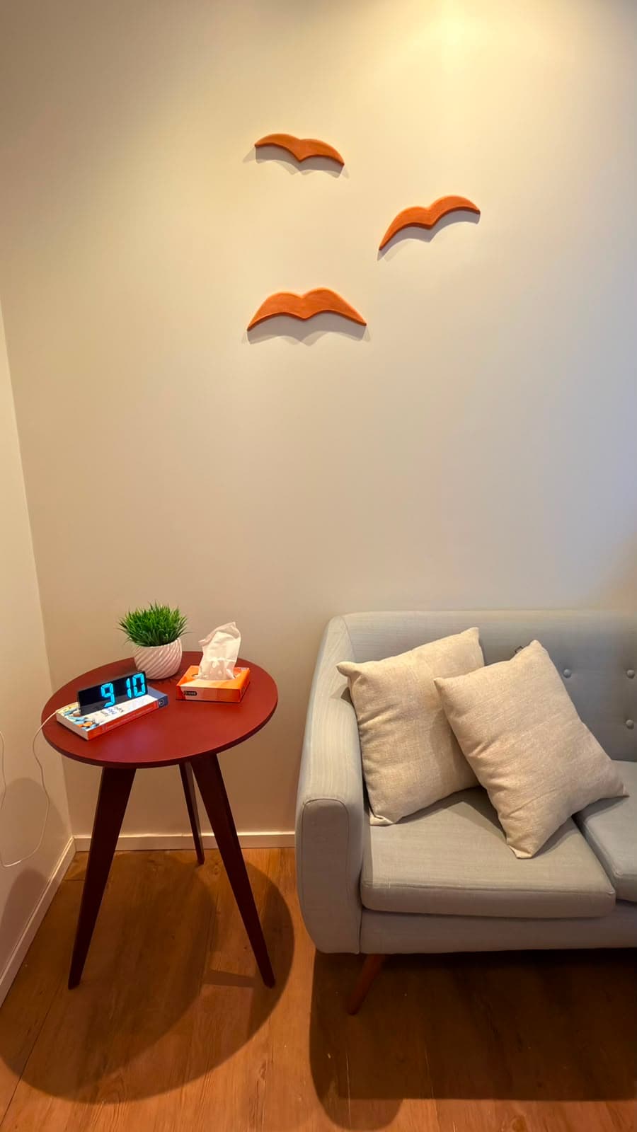 Sofá cinza com almofadas, mesa lateral com planta e relógio, e pássaros decorativos