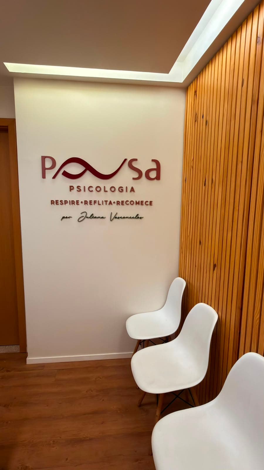 Parede da recepção com o logo em relevo, painel ripado de madeira e cadeiras de espera